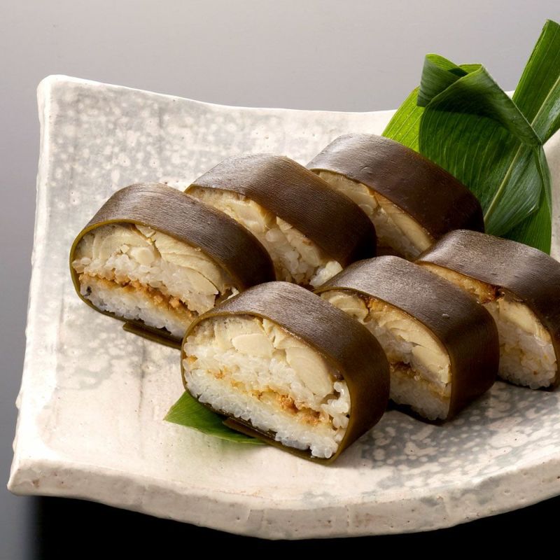 ６つにカットされた焼鯖ずしの断面（昆布や鯖の身、お米）が見え、笹を敷いたお皿に並んで盛り付られています。