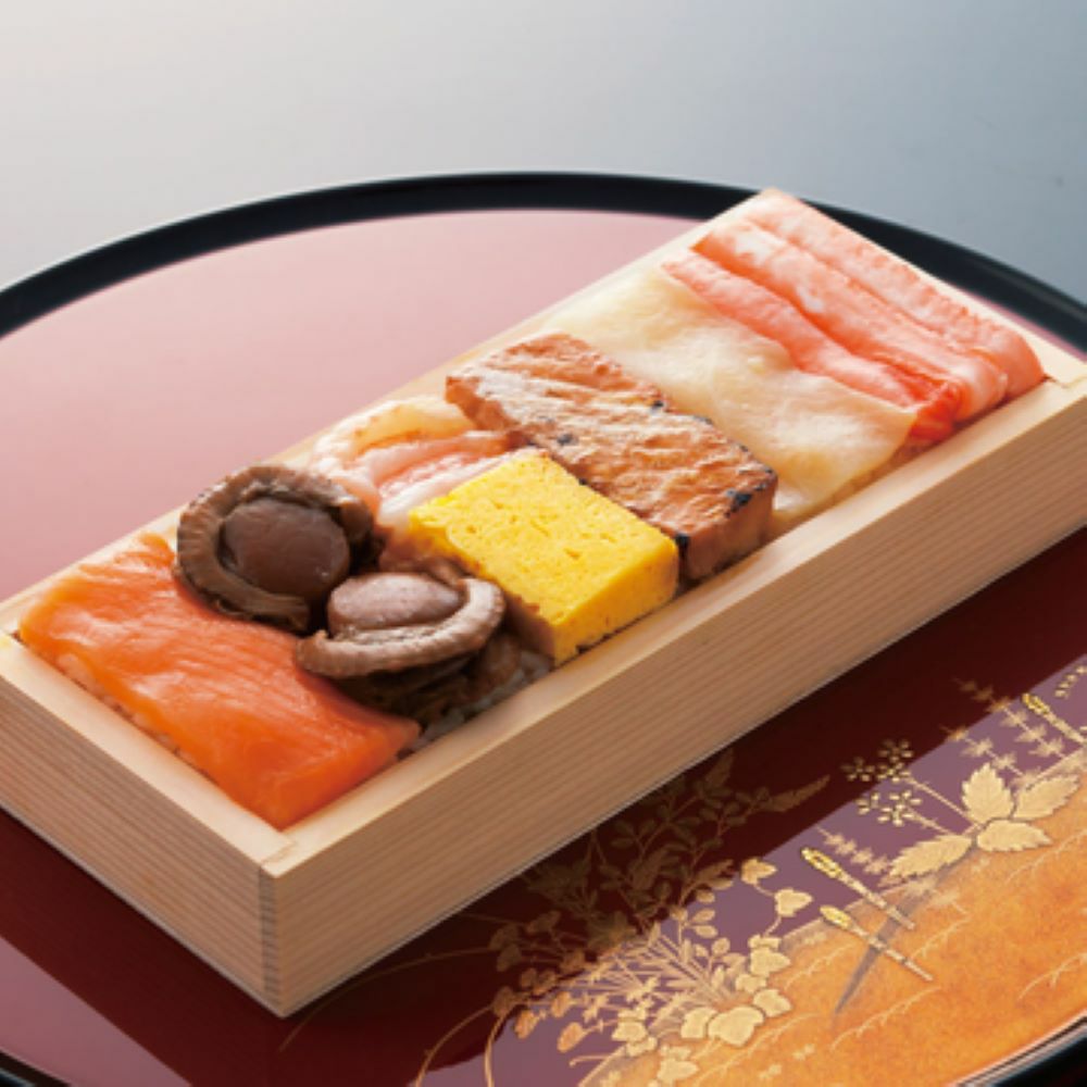木箱の中に七つの食材（鱒・ほたて・甘えび・玉子・鱒ハラミ・鰤・蟹）が美味しそうに並んだ押し寿司の画像。