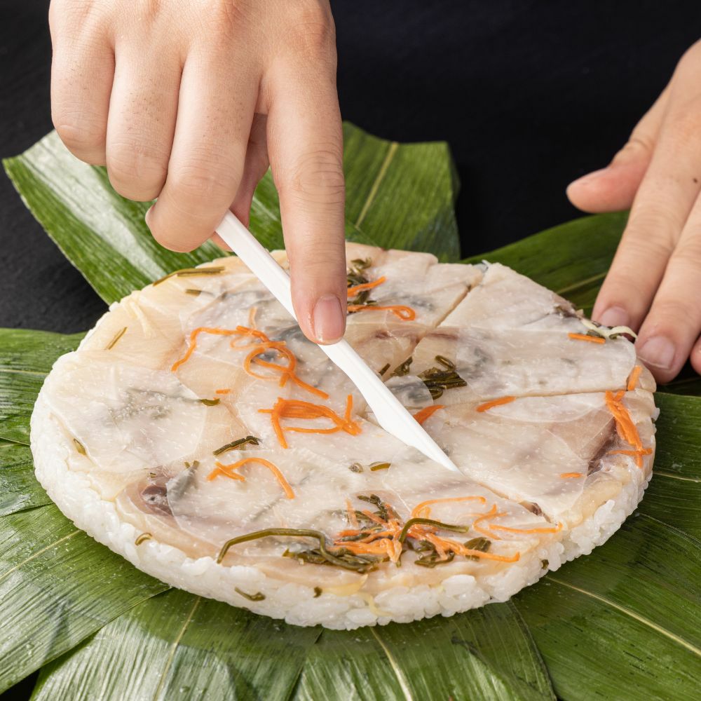 ぶりのすしをプラスチックナイフでカットしている画像。