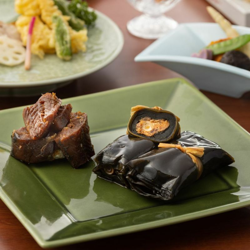 うま煮数種類がカットされお皿に盛りつけられ、その他のおかずと並んだ食卓イメージの画像です。