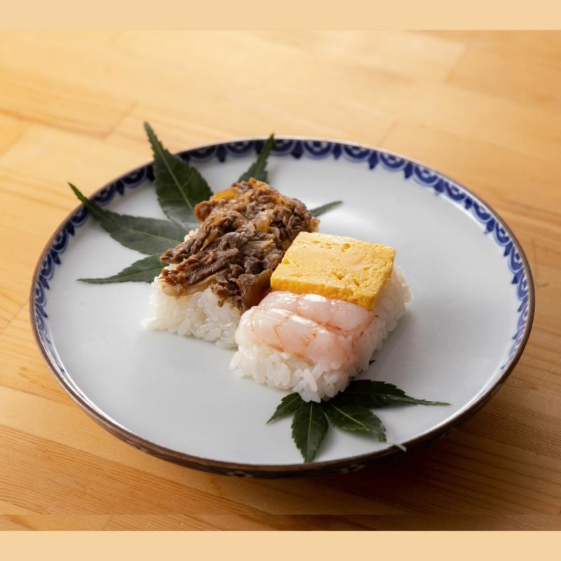 Rejyu（レジュウ）の氷見産牛すきやきと甘えびと玉子がお皿に盛りつけられているイメージ写真です。紅葉を敷いた上に盛りつけられています。